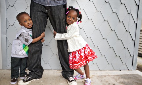 girl and boy toddler hug father's legs