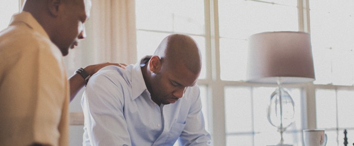 An older man prays over a younger man