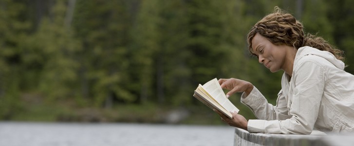 Mature woman lying on pier reading book, side view