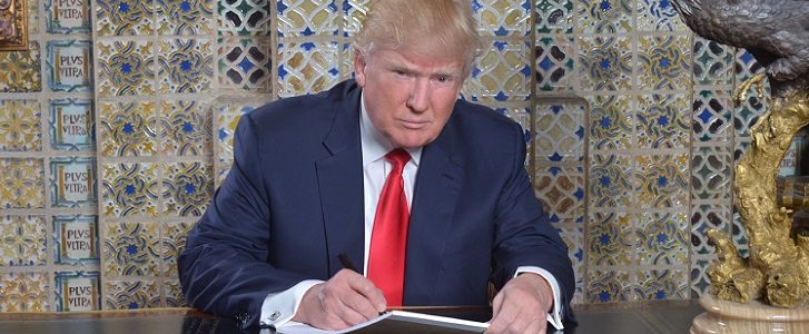 Donald Trump posing for a photograph while signing a document